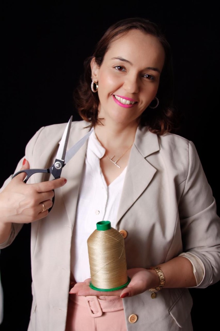 Fabiana Ribeiro sorrindo, com um cone de linha dourada e uma tesoura nas mãos